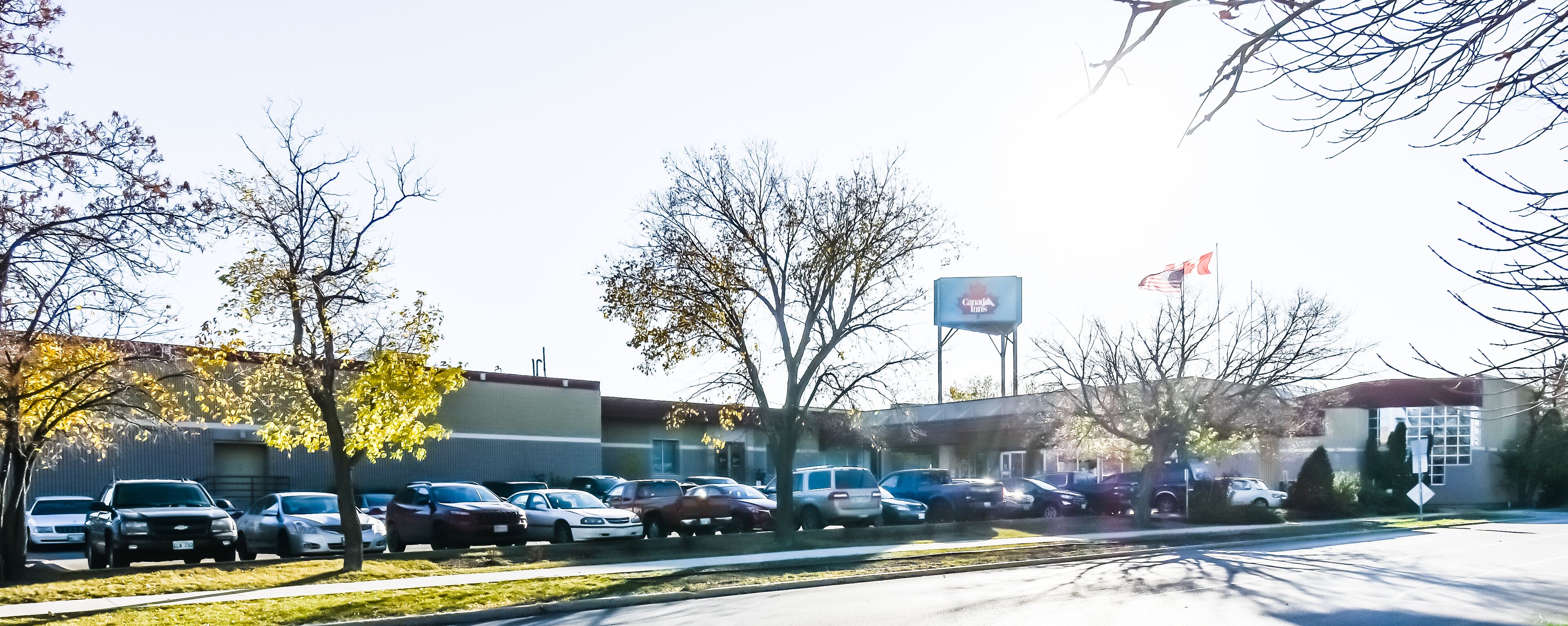A parking lot with various cars, trees, and a building with a sign that reads "Canada Inns".