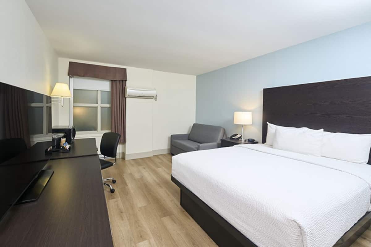 A hotel room with a large bed, a desk with a chair, a small sofa, and a window with curtains.