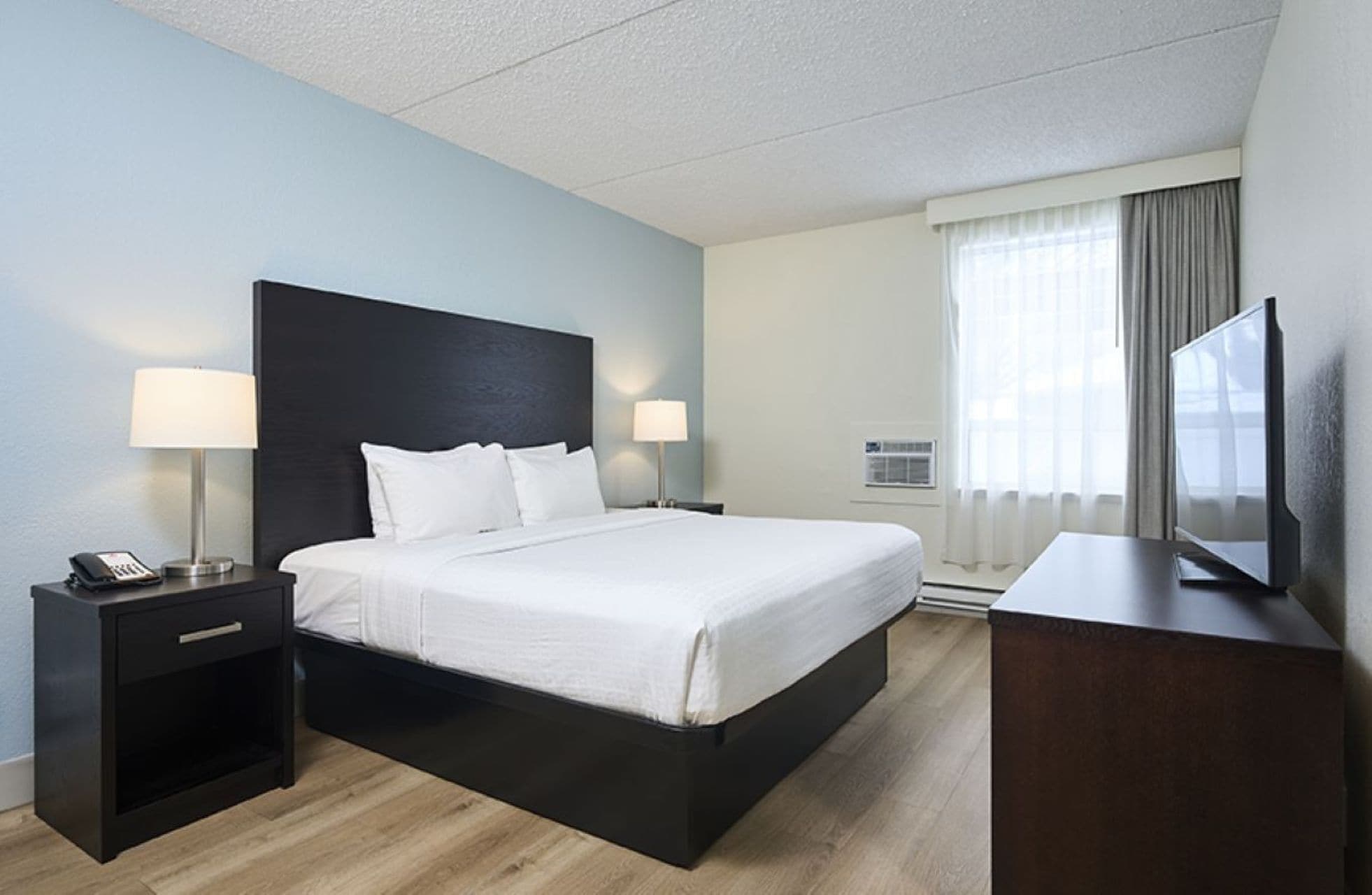 A hotel room with a bed, bedside lamps, a desk with a TV, and a telephone.