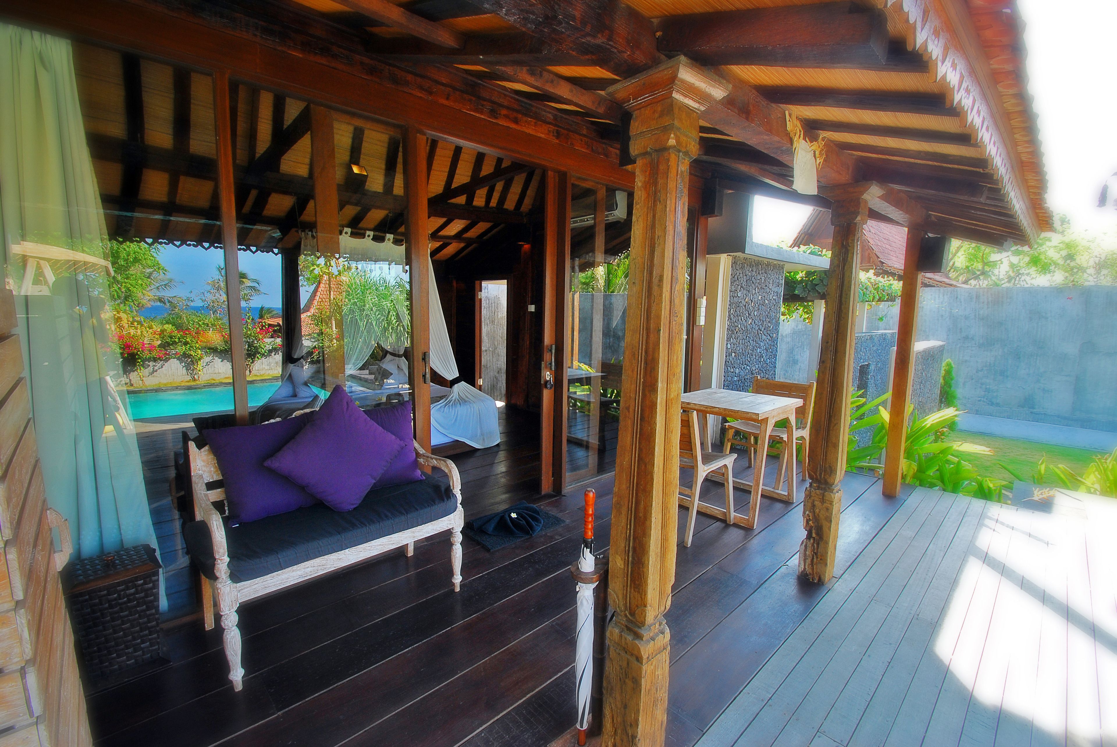 A wooden deck with a sofa and chairs, a table, and a view of a swimming pool and greenery.
