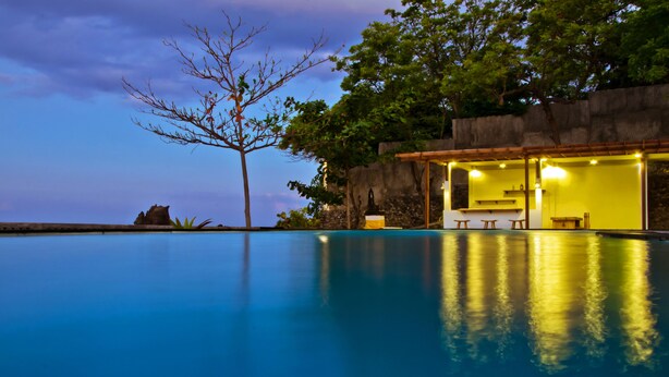 A serene swimming pool at dusk with a wooden structure and a tree nearby. - KajaNe Tulamben (Kubu)