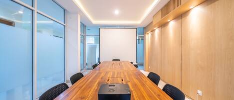 A conference room with a wooden table, black chairs, a projector, and glass walls.