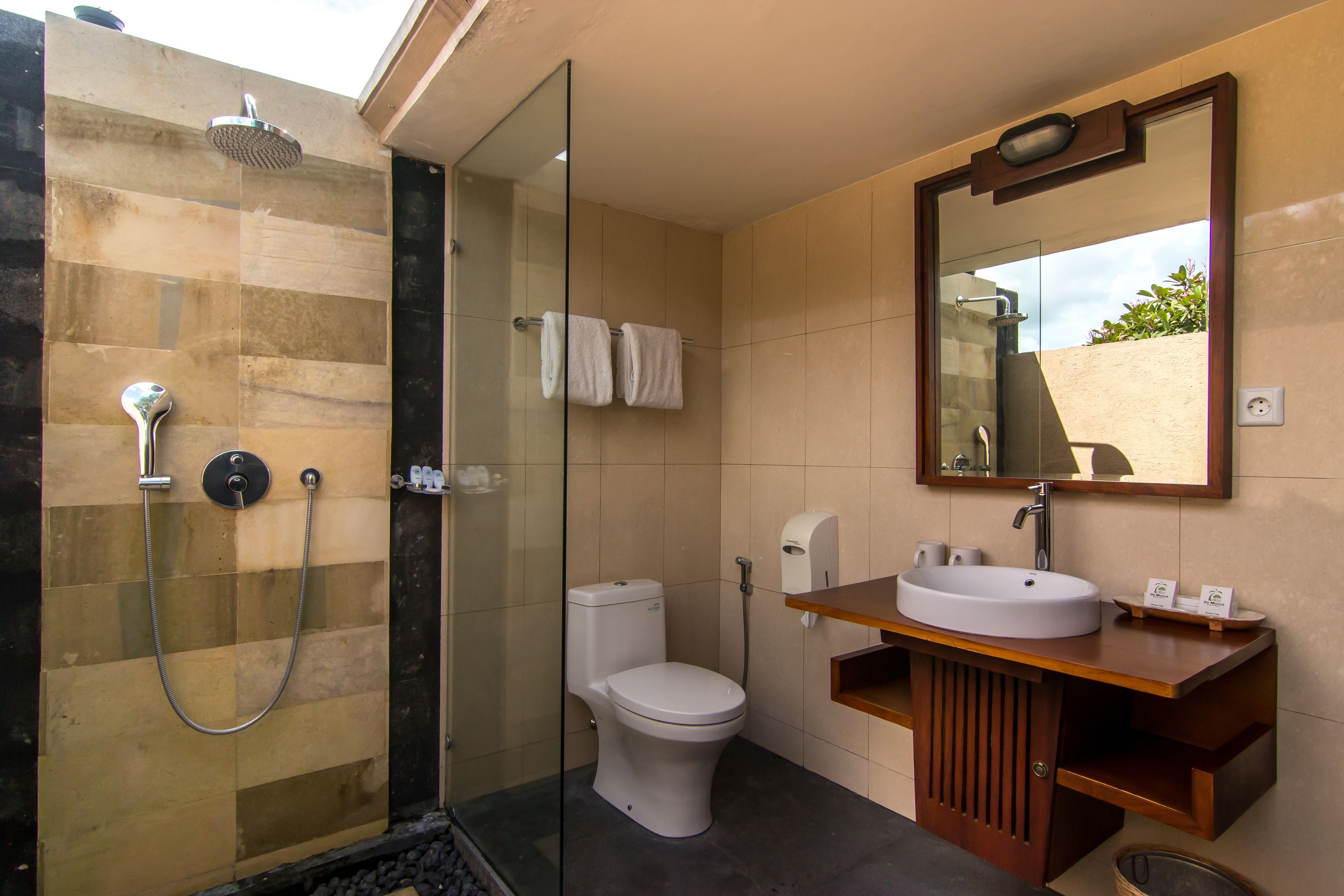 Un bany amb dutxa de vidre, vàter, un lavabo amb mirall i un paraigua de tovalloles.