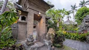 A traditional stone structure with a thatched roof, surrounded by lush greenery and a paved pathway. - De Munut Balinese Resort & Spa (Ubud)