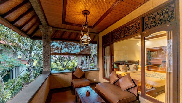 A cozy, well-lit room with a wooden ceiling, a large window offering a view of the outdoors, and a seating area with a sofa and a table. - De Munut Balinese Resort & Spa (Ubud)