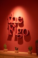 Una pared con el texto "Eligo" iluminado en letras rojas, y tres cactus en macetas sobre un estante de madera.