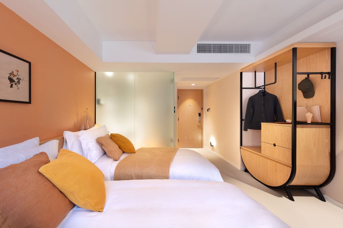 A hotel room with two beds, a wardrobe, and a coat rack.