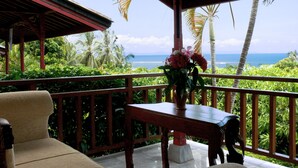 A wooden deck with a table and chairs, overlooking a tropical landscape with palm trees and the ocean. - Puri Bunga Senggigi (Senggigi)