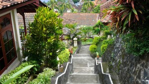 A staircase leading to a building with a tiled roof, surrounded by lush greenery and a view of the ocean. - Puri Bunga Senggigi (Senggigi)