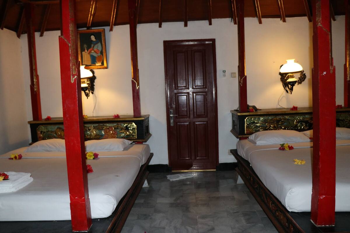 A hotel room with two beds, a wooden door, and wall-mounted lamps.