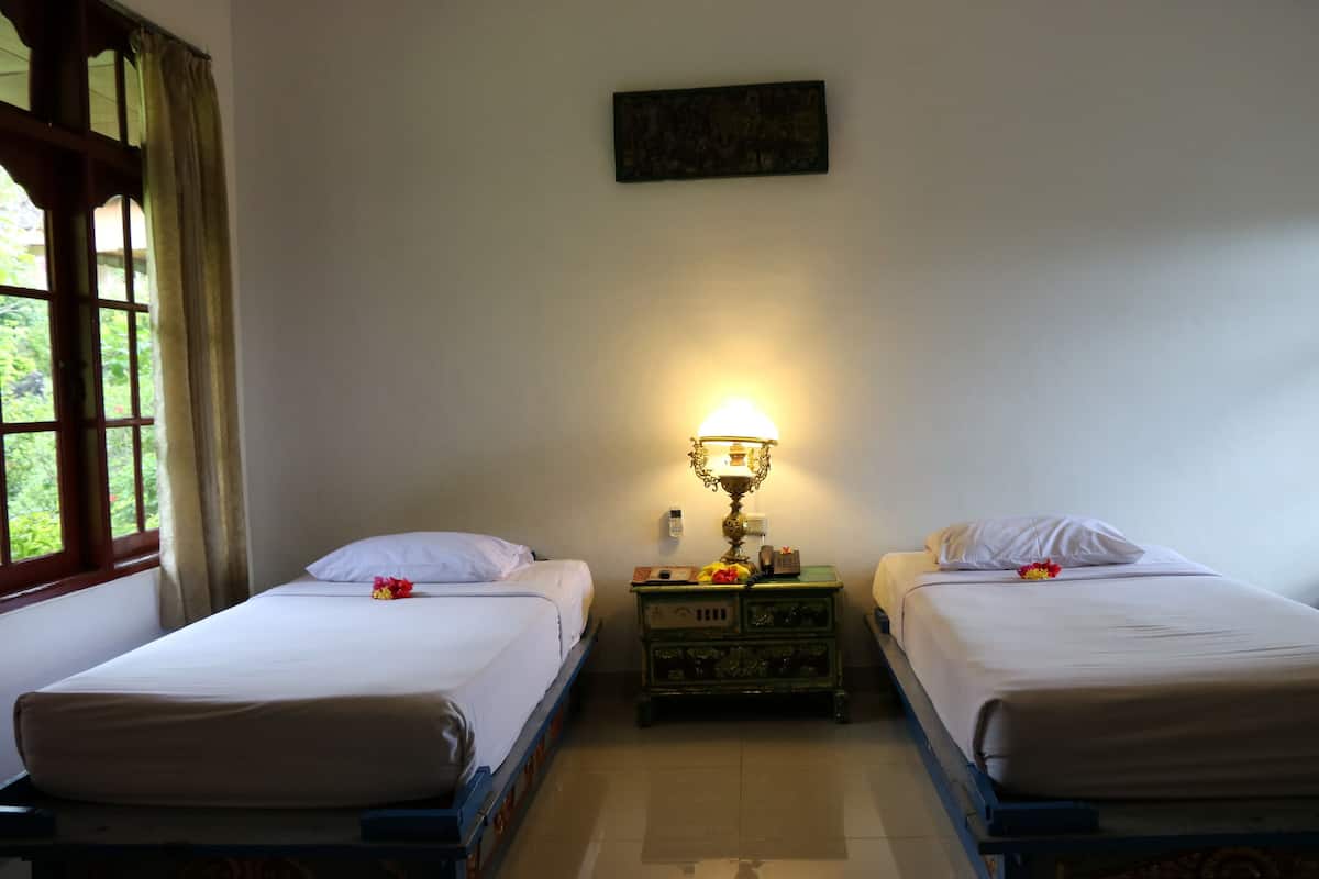 A room with two single beds, a nightstand with a lamp, and a window with curtains.