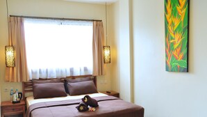 A neatly made bed with brown bedding, a nightstand with a coffee pot, and a painting on the wall.