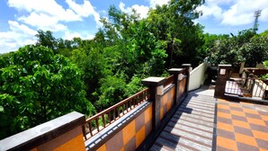 A balcony with a checkered floor and a railing, surrounded by lush greenery.