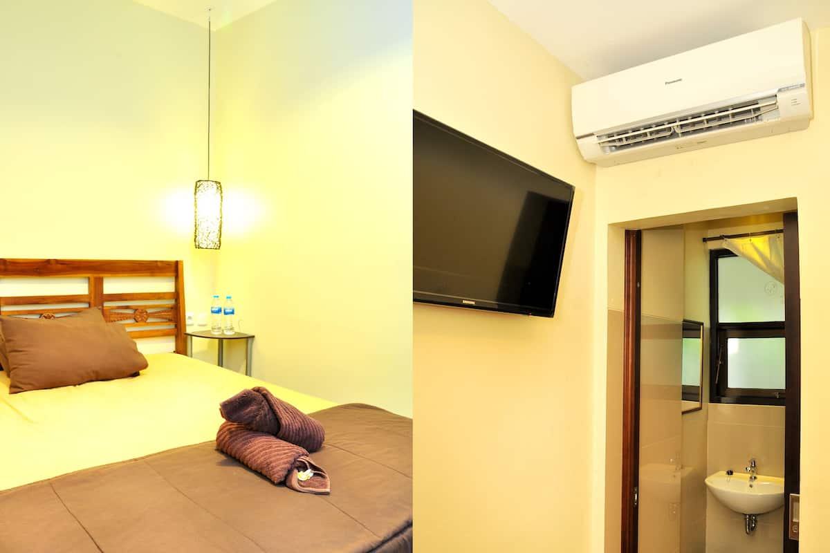 Een hotelkamer met een bed, een nachtkastje met waterflesjes, een televisie en een airconditioning.