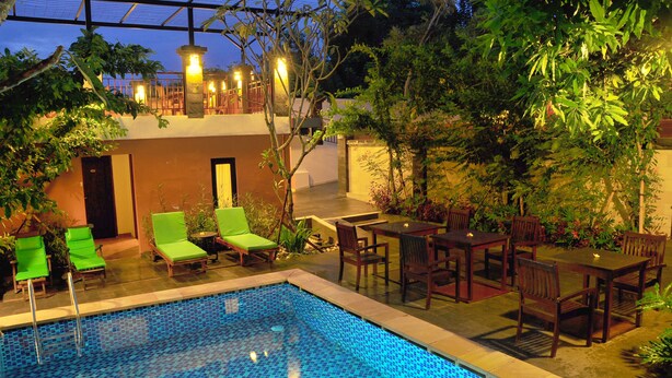 A pool area with lounge chairs and tables, surrounded by greenery and a covered seating area.