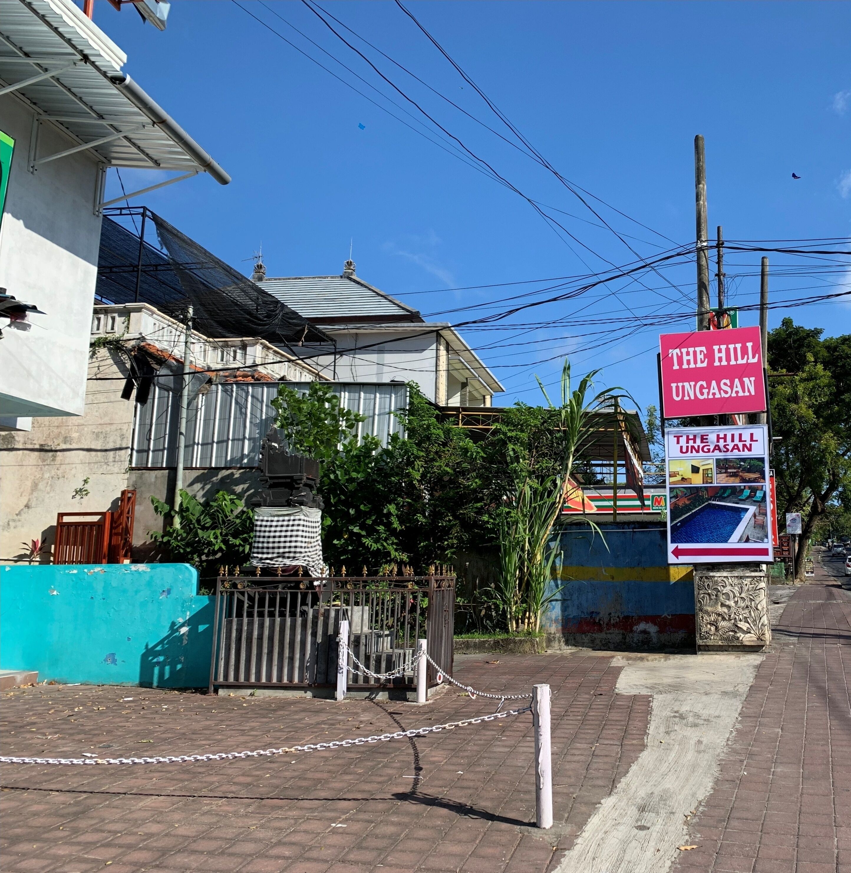 A sign for "The Hill Ungasan" with a view of a residential area, a gated entrance, and a brick pathway.