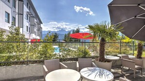 An outdoor patio with round tables and wicker chairs, overlooking a pool and mountains. - Appart'City Confort Grenoble Inovallée (Montbonnot-Saint-Martin)