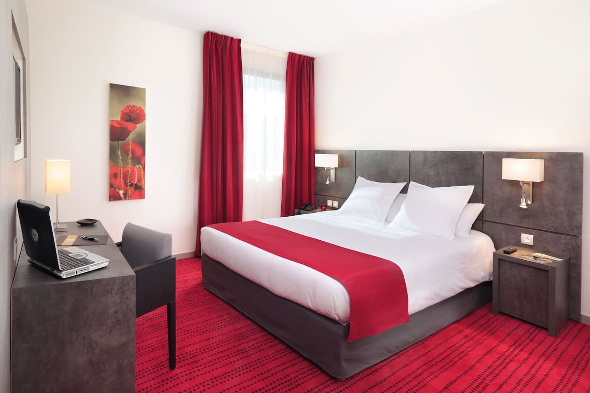Hotellihuone, jossa on suuri sänky, työpöytä kannettavalla tietokoneella ja punainen matto.
