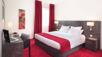 A hotel room with a large bed, a desk with a laptop, and a red carpet.