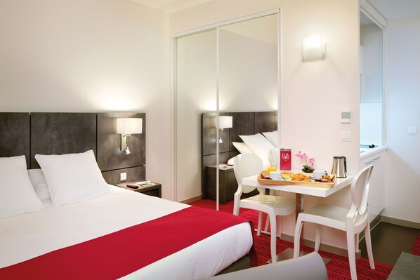 A hotel room with a large bed, a desk with a tray of breakfast items, a chair, and a mirror.