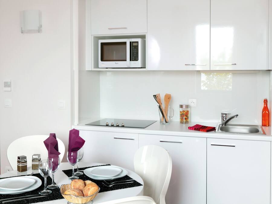 A modern kitchen with white cabinets, a microwave, a sink, and a dining area with a table set for two.