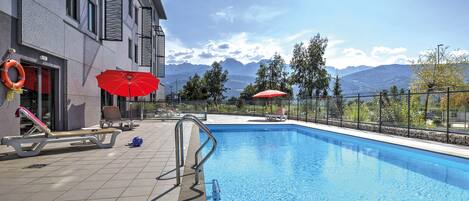 Ein Schwimmbecken mit Bergblick, einem Rettungsring und einem roten Sonnenschirm.