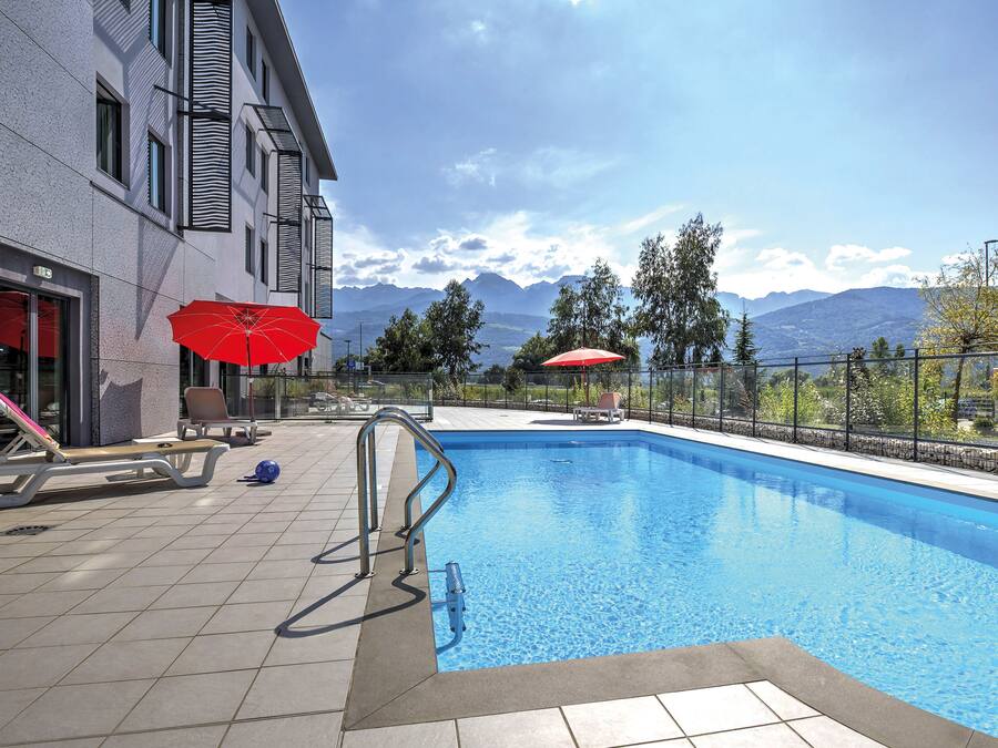 A swimming pool with a view of mountains, a lifebuoy, and a red umbrella.