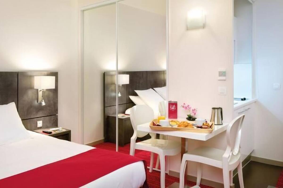 Hotellihuone, jossa on sänky, yöpöydät, työpöytä tuoleineen ja aamiaistarjotinpöytä.