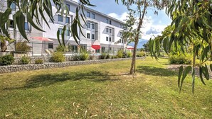 A modern building with a flat roof, large windows, and a stone retaining wall. - Appart'City Confort Grenoble Inovallée (Montbonnot-Saint-Martin)