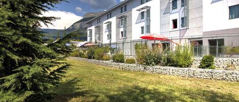 A modern hotel with a stone pathway, neatly trimmed grass, and red umbrellas.