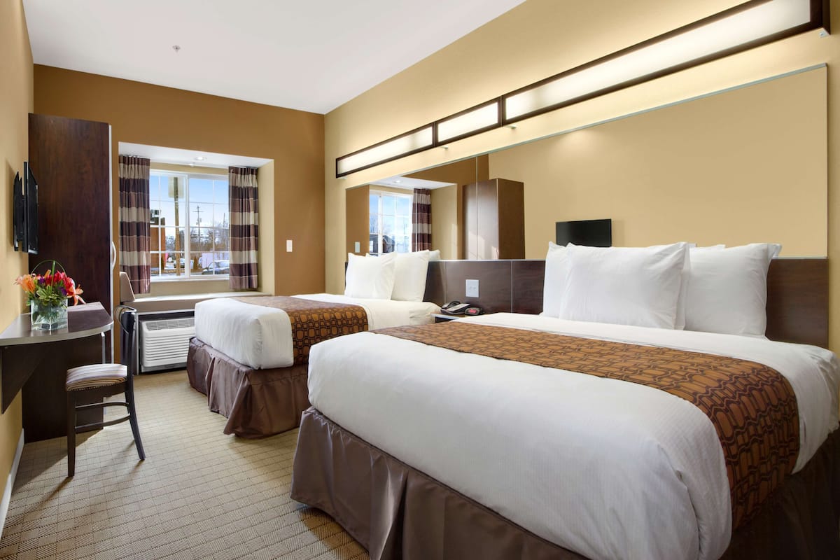 Ein Hotelzimmer mit zwei Betten, einem Schreibtisch, einem Stuhl, einem Fernseher und einem großen Fenster mit Vorhängen.
