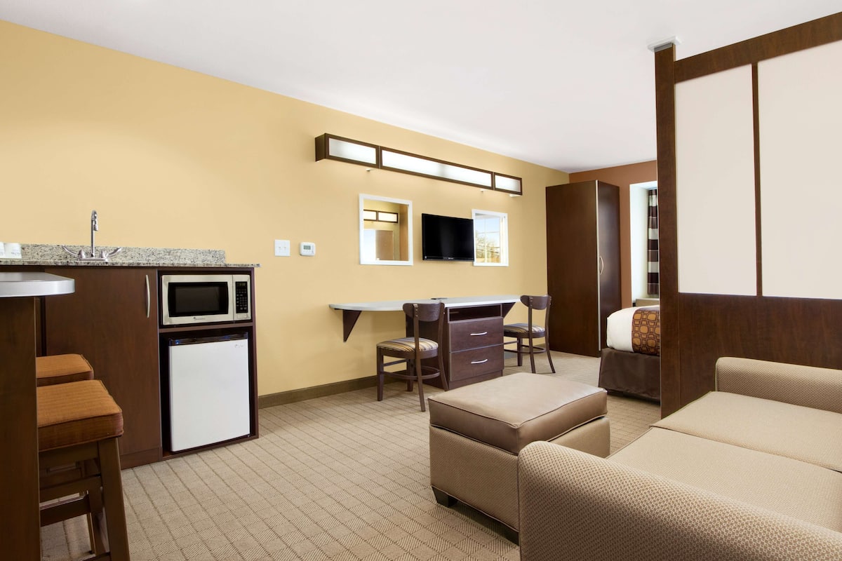 Ein kleines Hotelzimmer mit Küchenzeile, einem Flachbildfernseher, einer Couch und einem Bett.