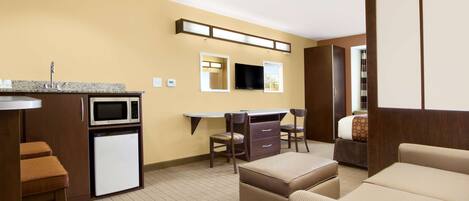A compact hotel room with a kitchenette, a flat-screen TV, a sofa, and a bed.