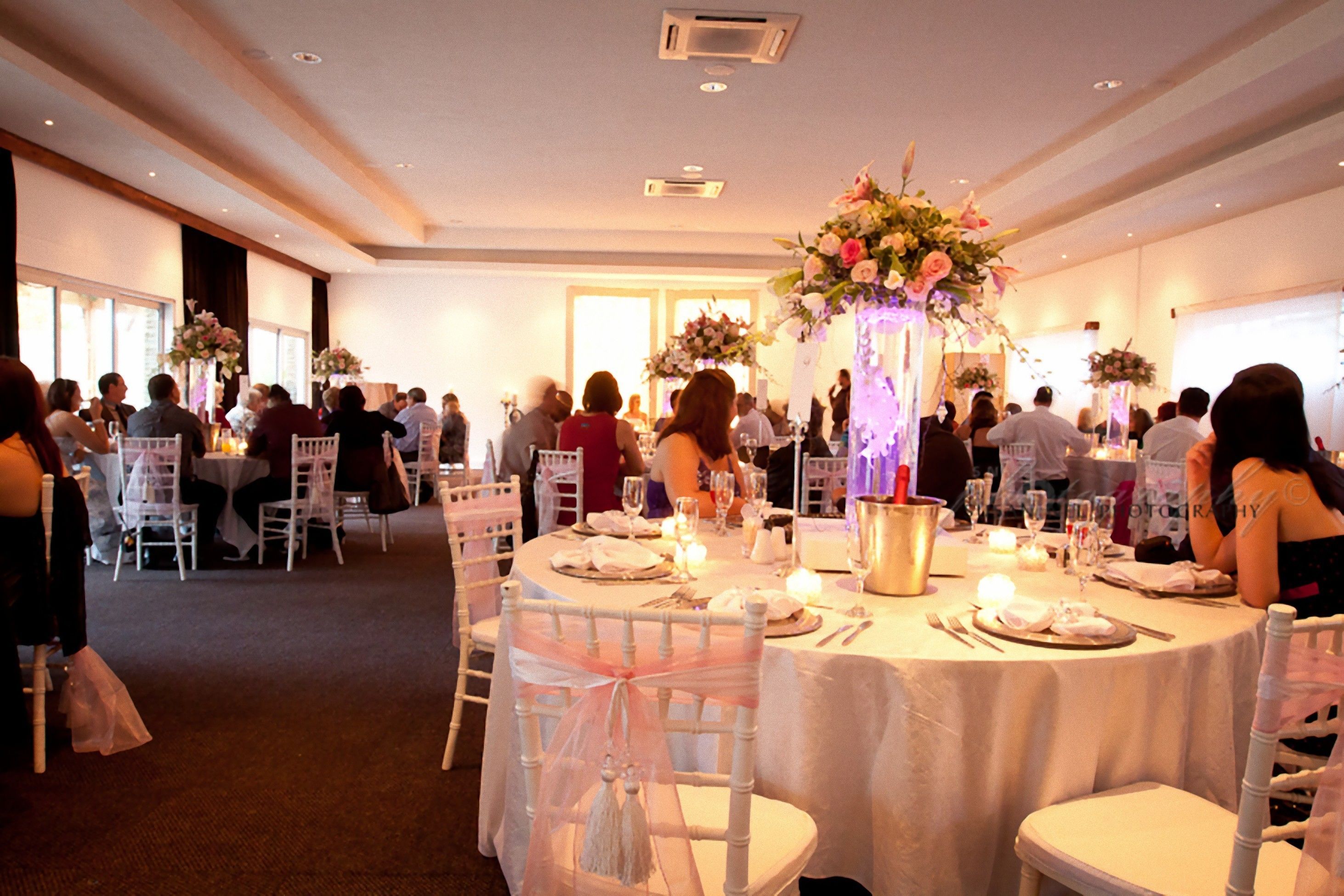 Un salón de banquetes con mesas redondas, sillas blancas y centros de mesa florales.