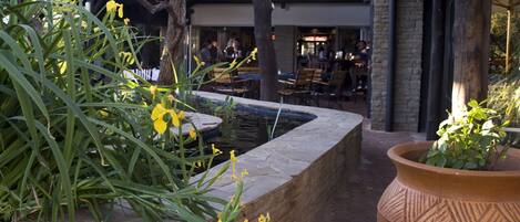 An outdoor patio area with a stone planter, a small water feature, and a seating area with tables and chairs.