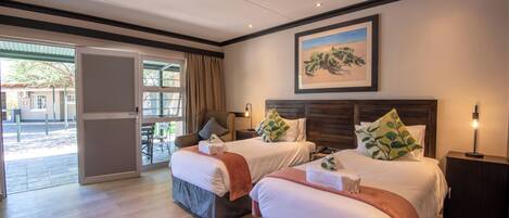 Habitación de hotel con dos camas, un ventanal grande, una puerta que da al exterior y un cuadro en la pared.