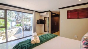 Ein Hotelzimmer mit einer großen Glasschiebetür zu einer Terrasse, einem Bett mit grüner Bettdecke und einem an der Wand montierten Flachbildfernseher.