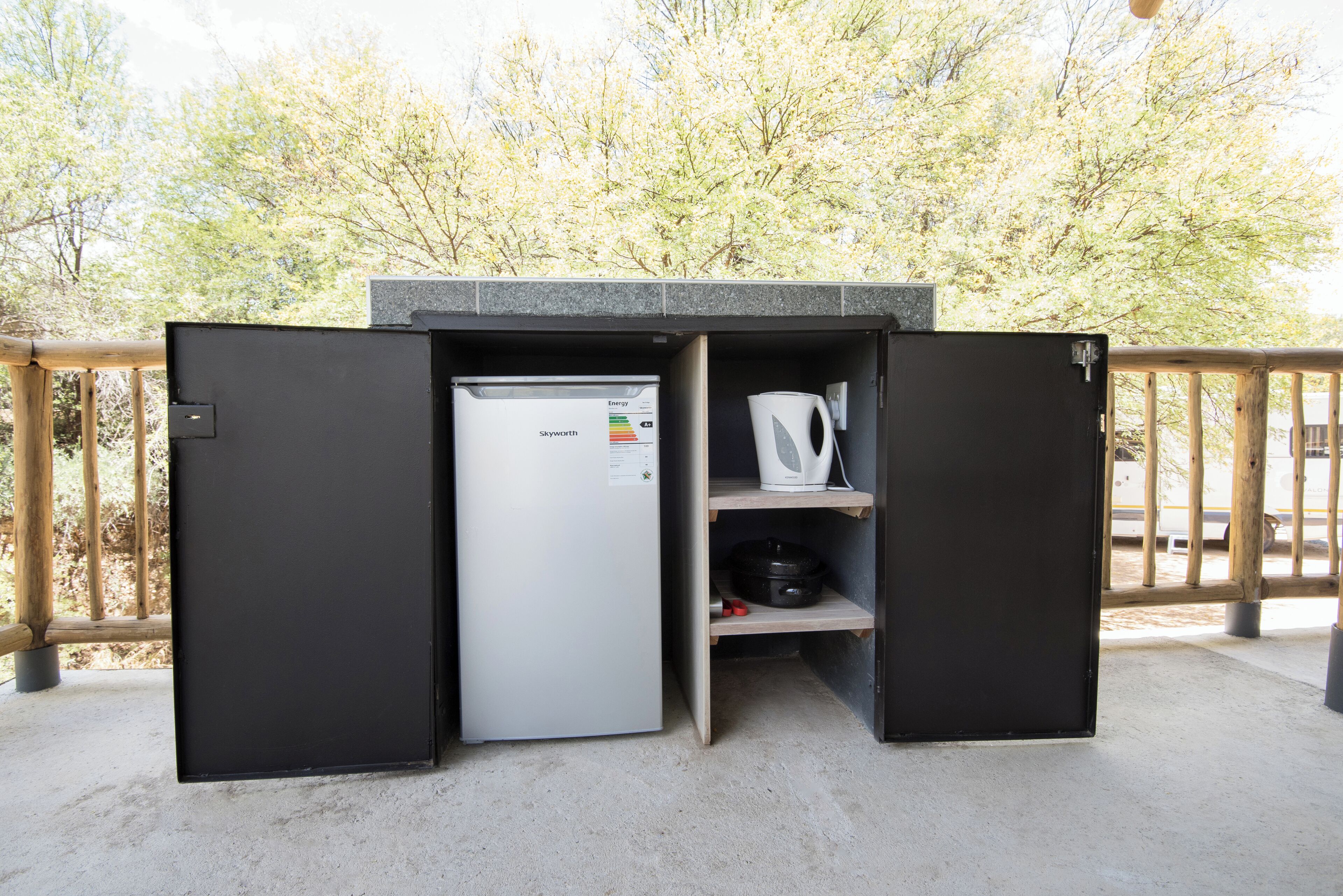 A compact outdoor kitchenette with a refrigerator, a kettle, and a coffee maker.