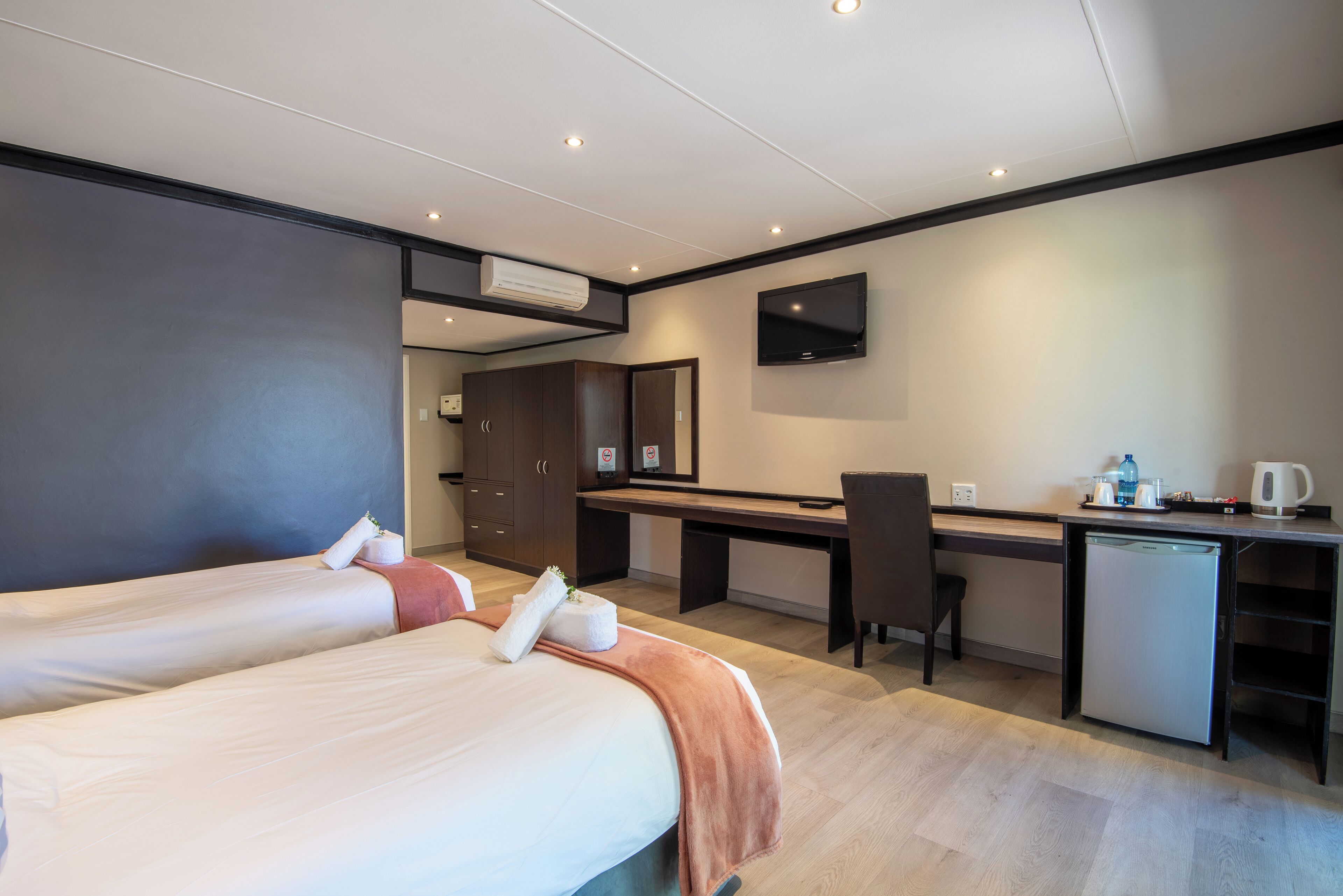 A hotel room with two beds, a desk, a chair, a small refrigerator, and a TV mounted on the wall.