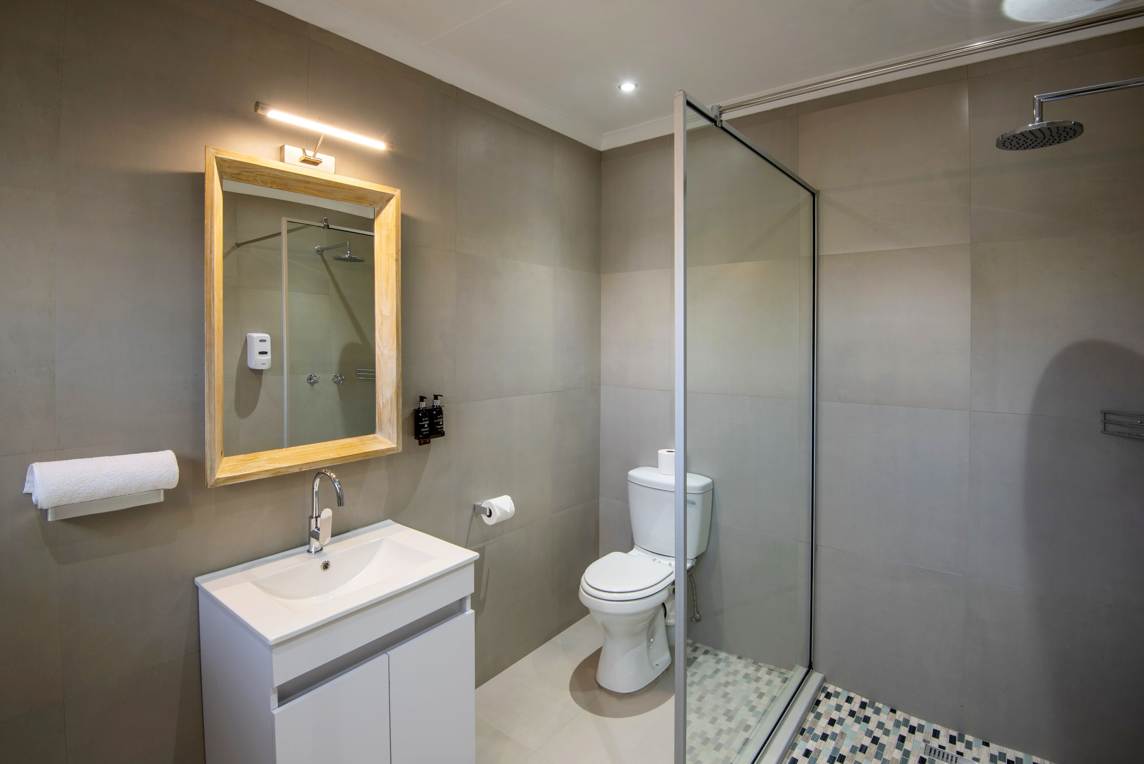 Un baño moderno con ducha de vidrio, lavamanos blanco y un inodoro.