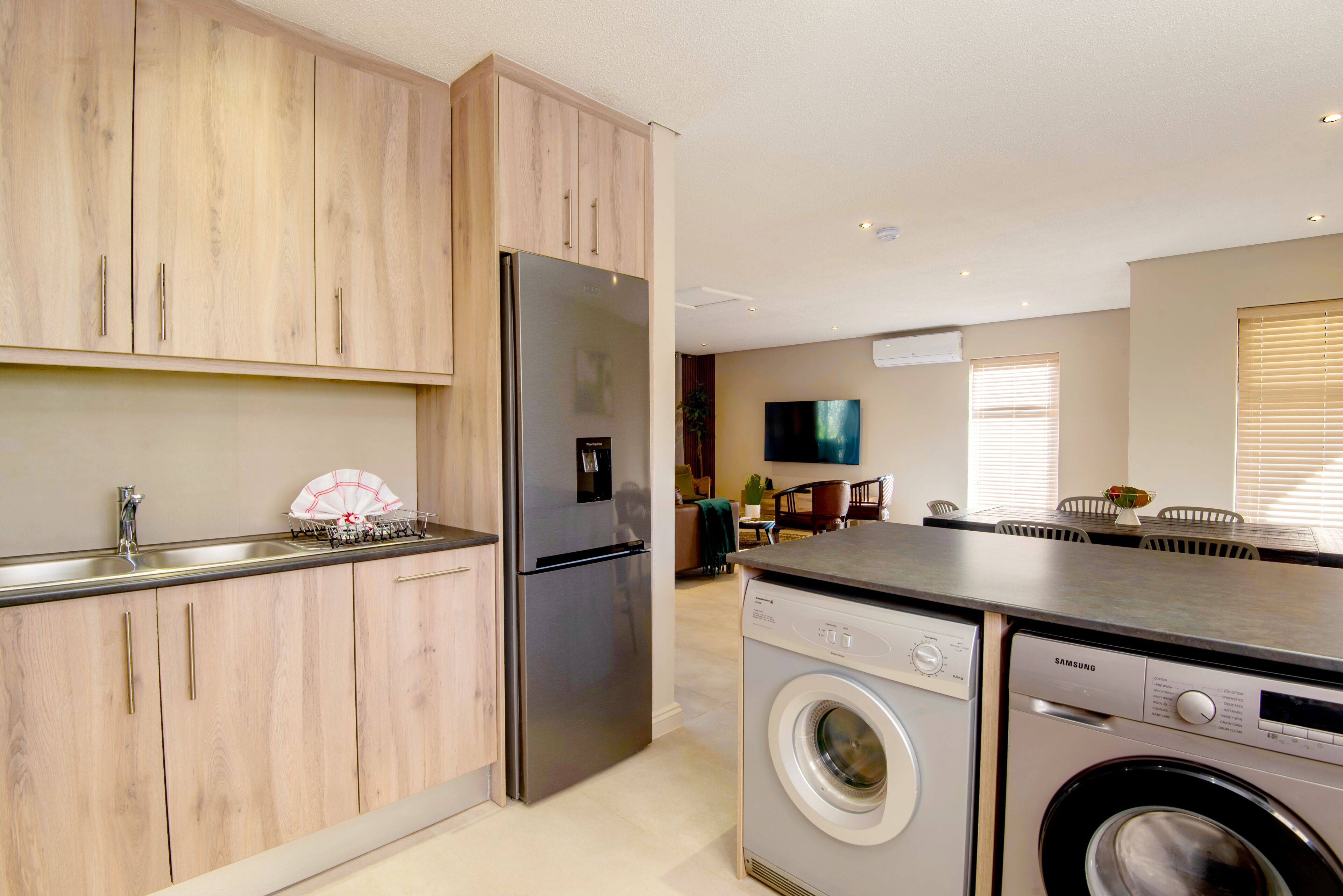 Une cuisine moderne dotée d’appareils électroménagers en acier inoxydable, de meubles en bois et d’un lave-linge et d’un sèche-linge intégrés.