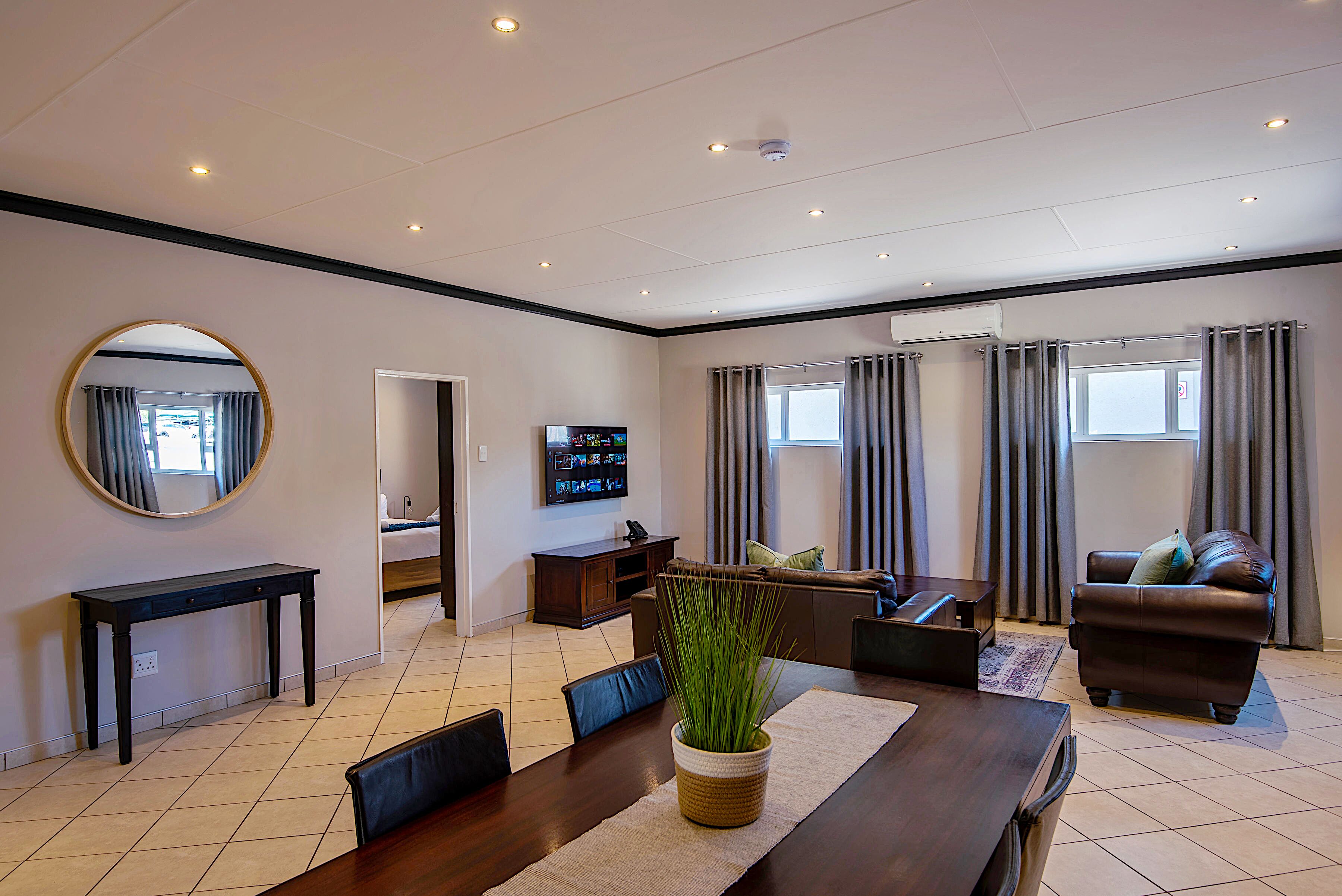 Una sala de estar moderna con una mesa de comedor, sofá, televisor y un espejo grande.