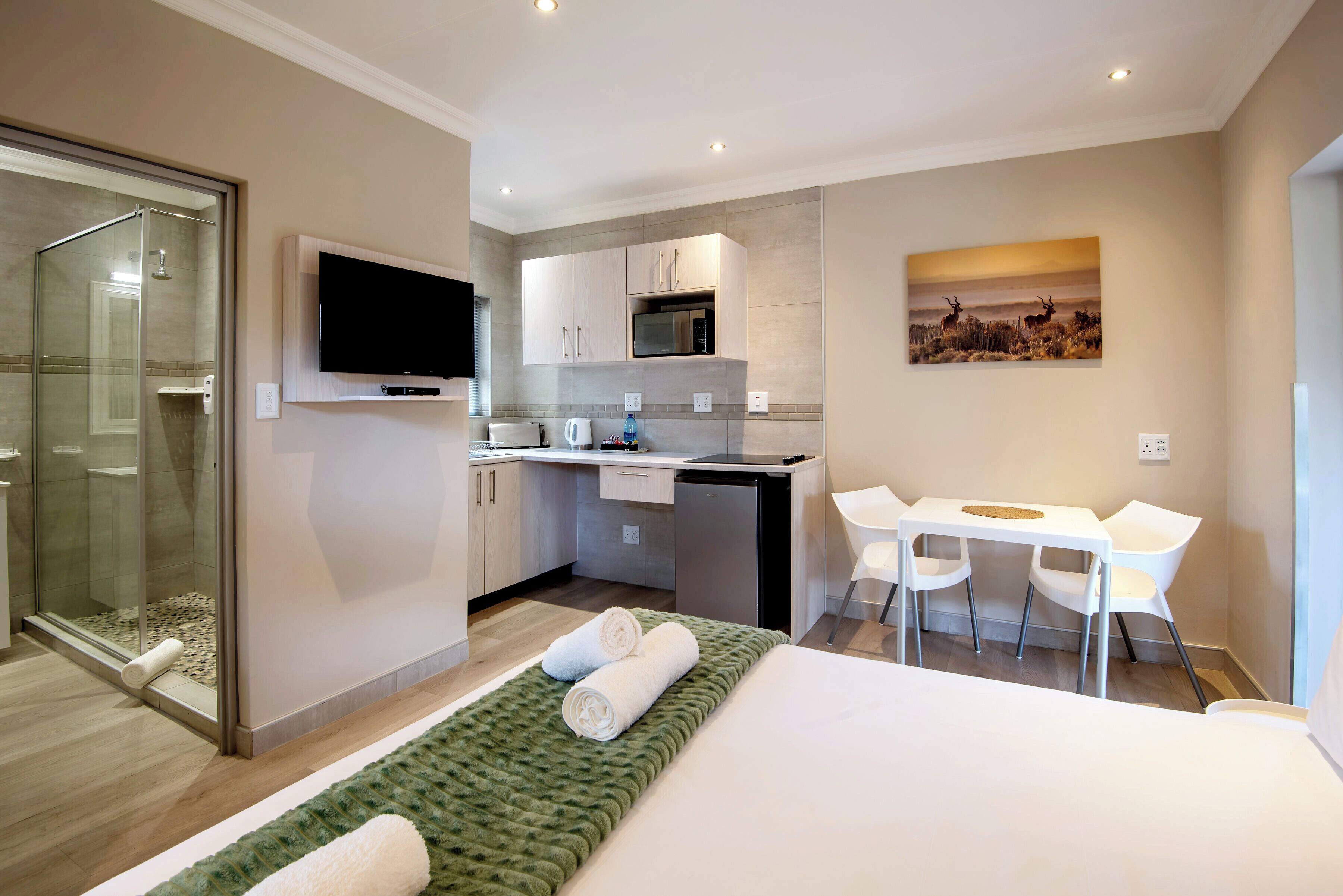 Habitación de hotel moderna con cama, escritorio, silla, televisor, microondas y cabina de ducha de vidrio.