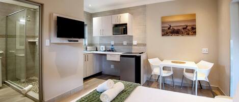 A modern hotel room with a bed, a desk, a chair, a TV, a microwave, and a glass shower enclosure.