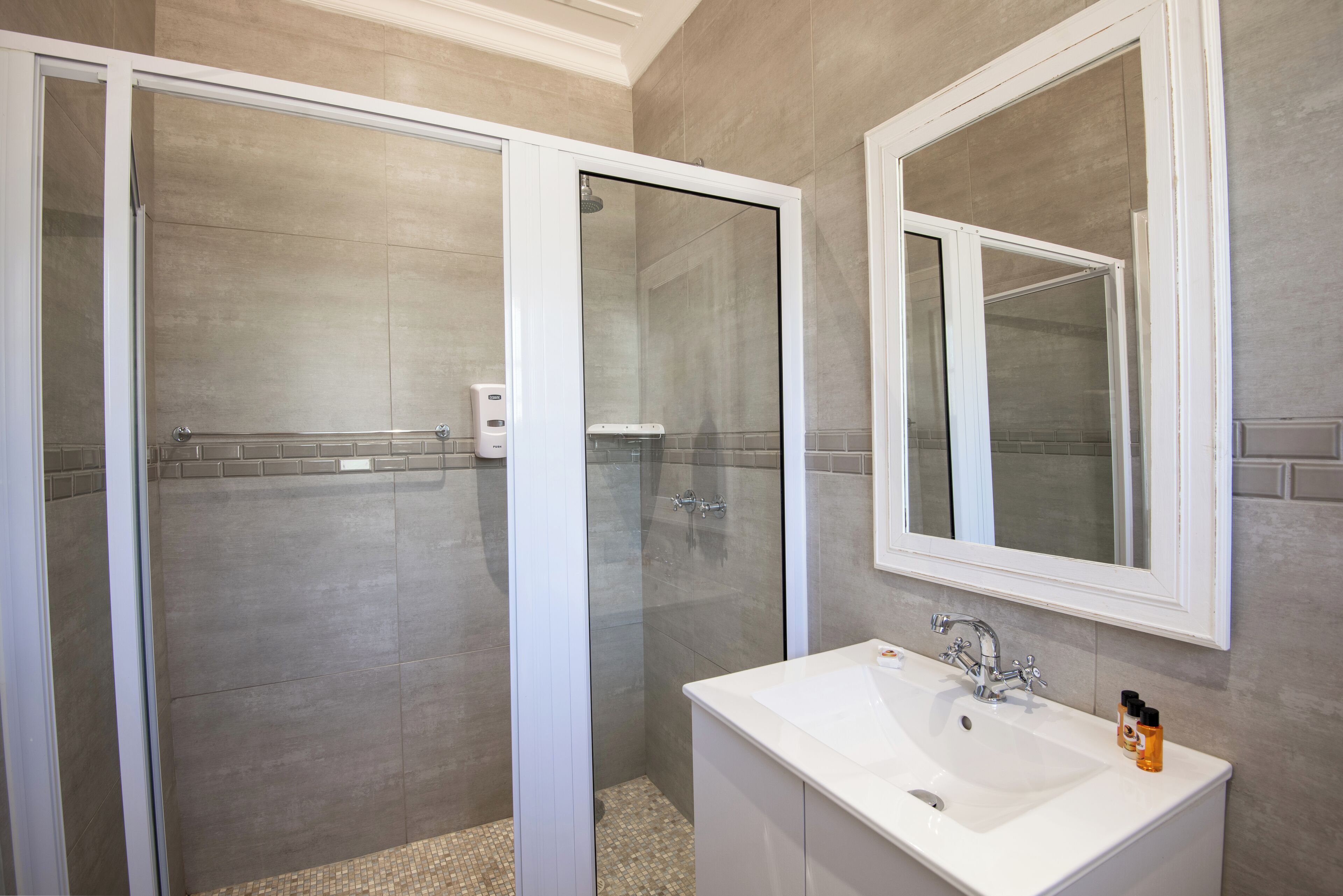 Un baño con ducha de vidrio, lavamanos blanco y un espejo grande.