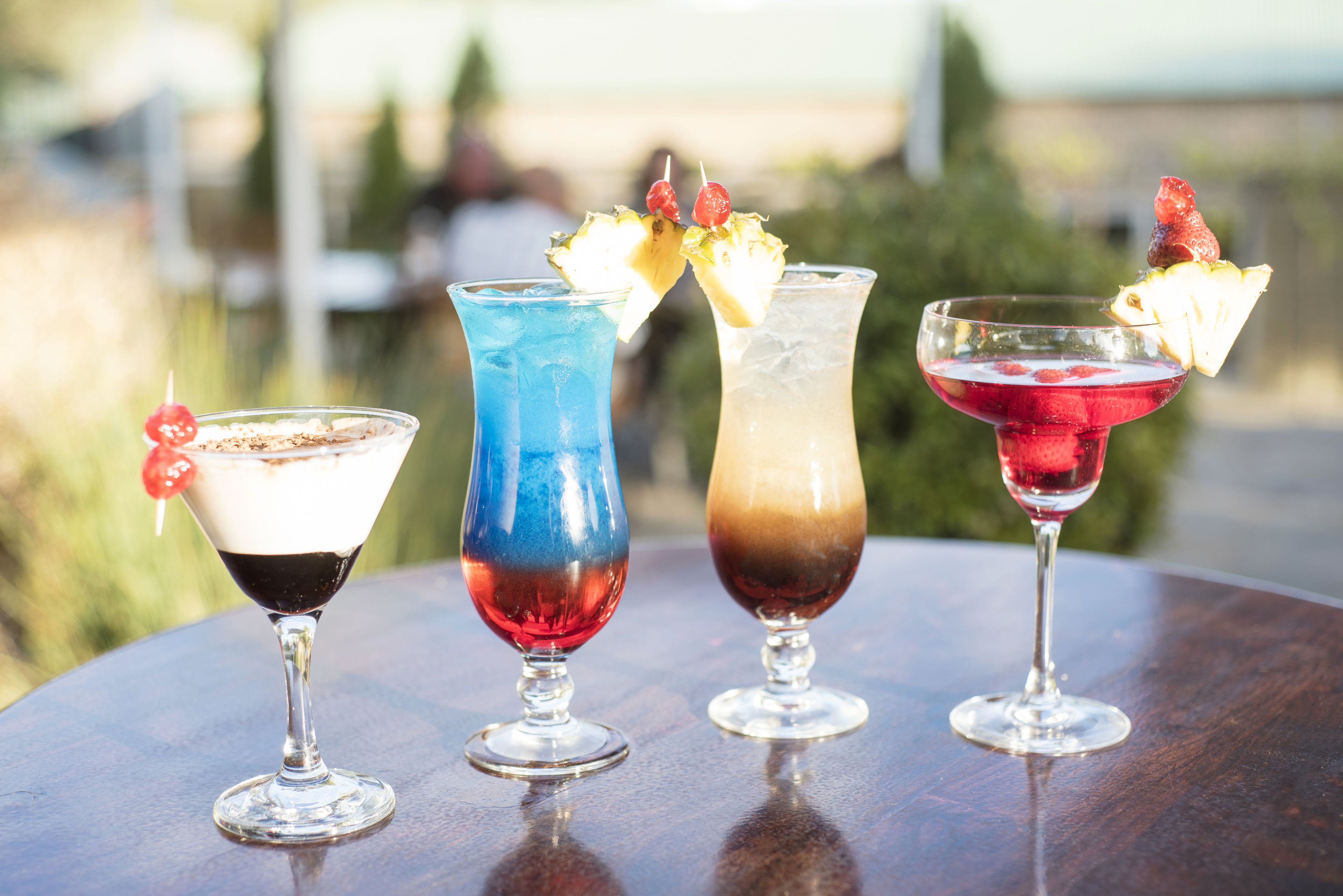 Four cocktails on a table with a blurred outdoor background.