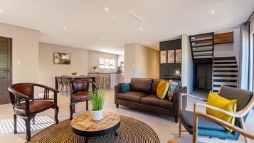 A modern living room with a brown leather sofa, a coffee table, and a dining area with chairs and a table.