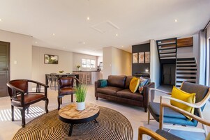 Una sala de estar moderna con un sofá de cuero marrón, una mesa de centro y una zona de comedor con sillas y una mesa.