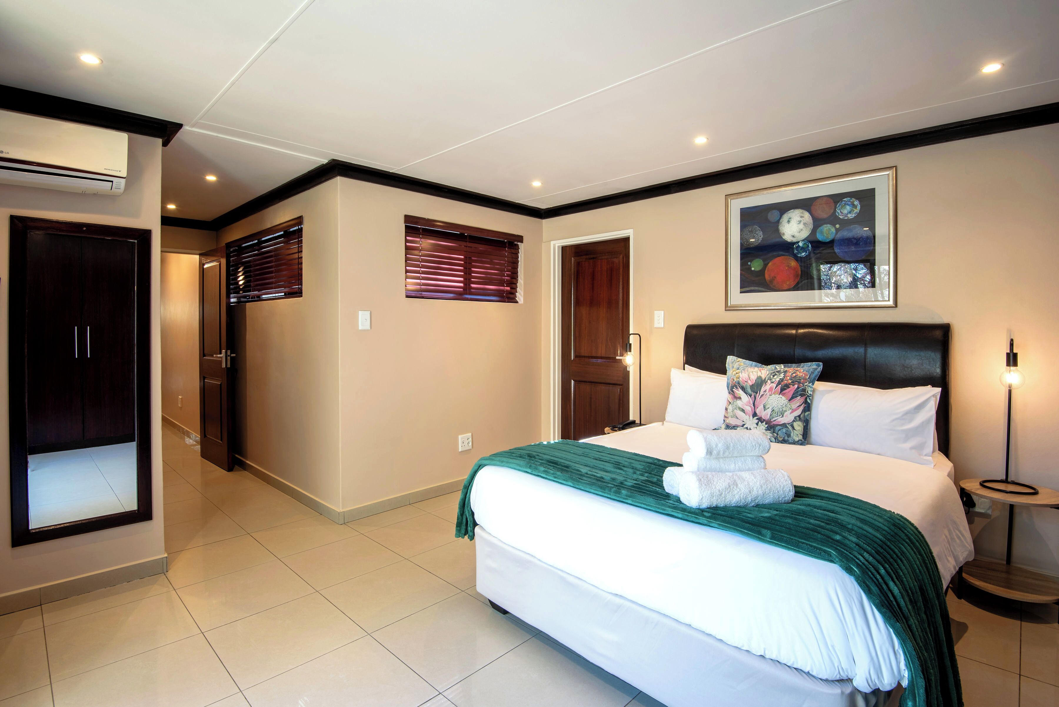 A hotel room with a large bed, a headboard, a wall-mounted artwork, and a bedside table with a lamp.