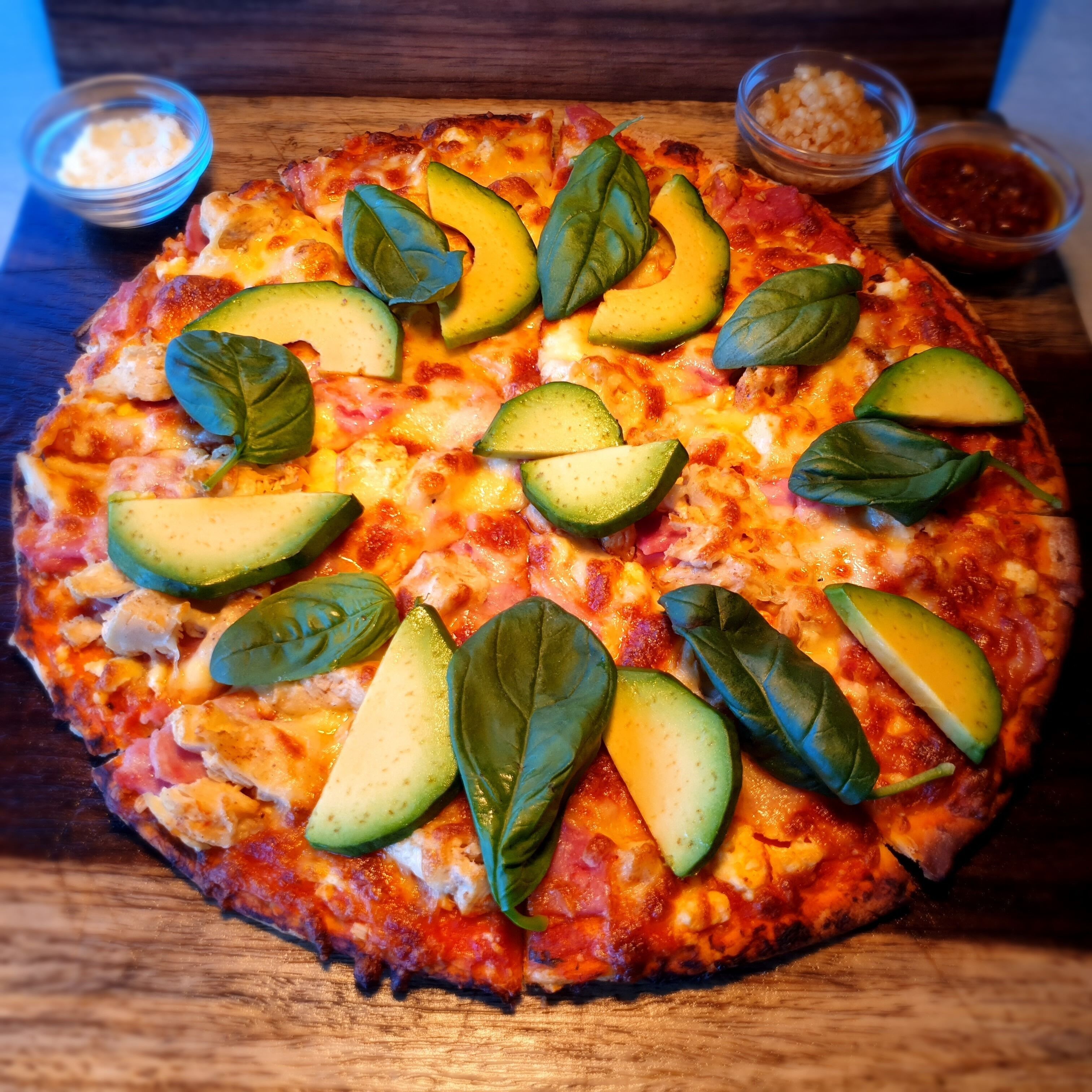 A pizza with avocado slices and basil leaves on a wooden board.